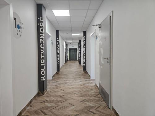 Jasny korytarz w Centrum Grawitacja prowadzący do gabinetów terapeutycznych i sal szkoleniowych, oznaczonych nazwami specjalistycznych obszarów terapii. 